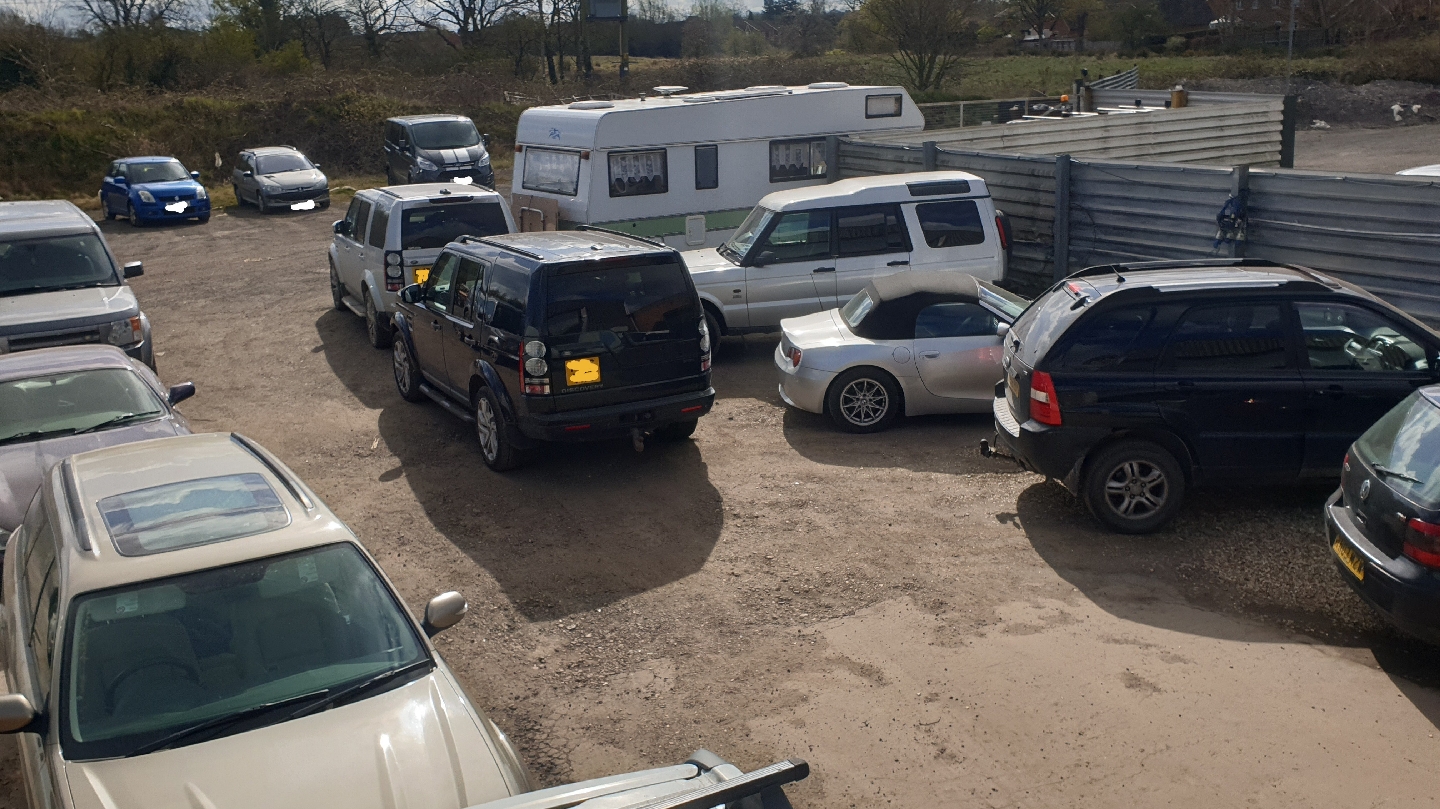 The yard at Manic Mechanic full of customers' Land Rovers, a Discovery and a BMW Z4, with a caravan behind