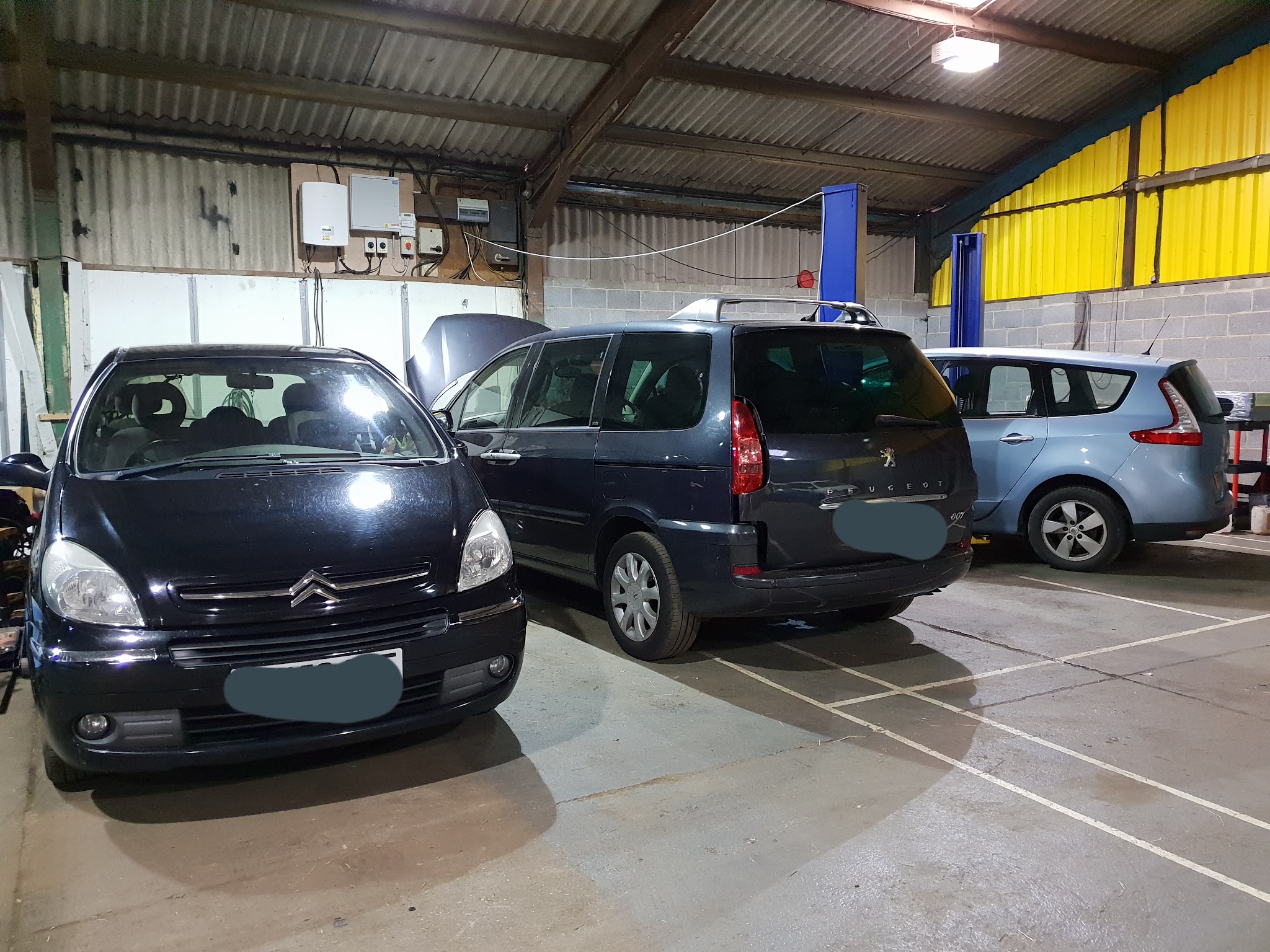 Workshop bays with a Citroen, a Peugeot people carrier and a Ford Galaxy in for work beside the blue lifts