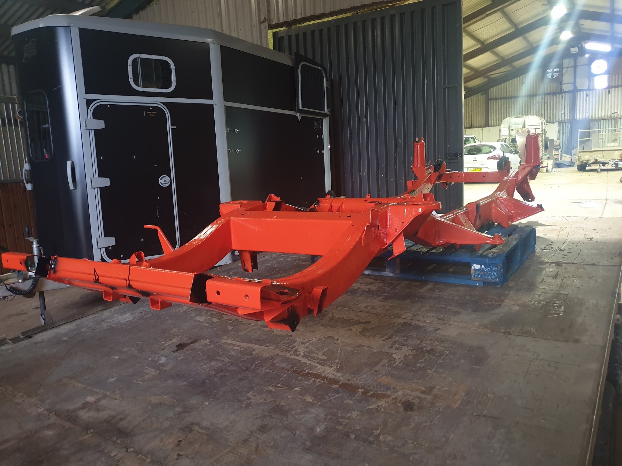 A freshly painted orange vehicle chassis on pallets inside the workshop