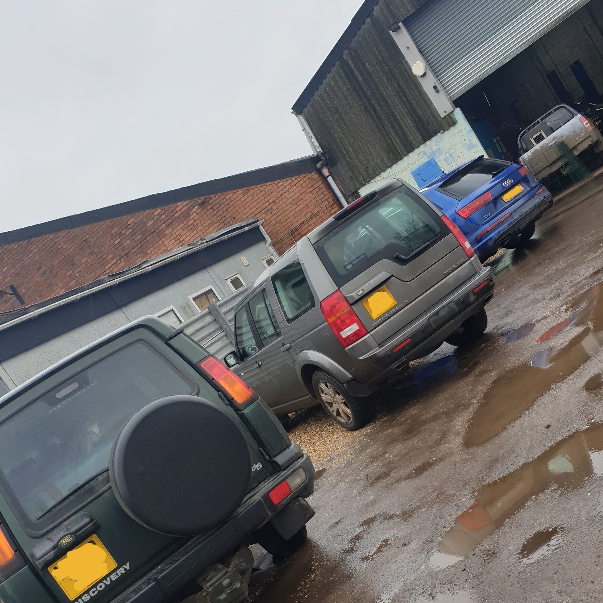 Two Land Rover Discoverys and an Audi outside the workshop units on a wet day